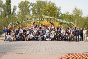 Group picture of ~75 conference participants against a green treeline