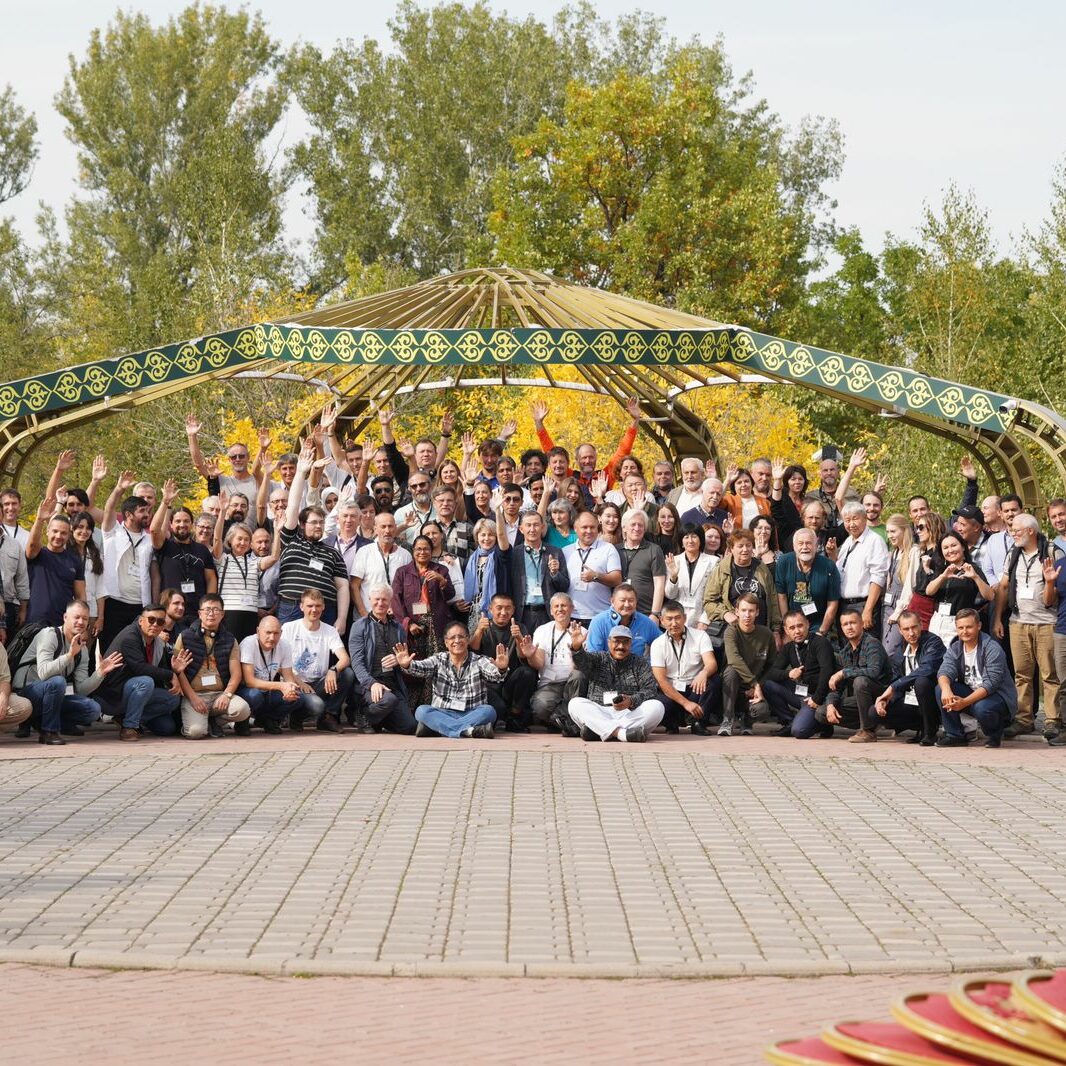Group picture of ~75 conference participants against a green treeline